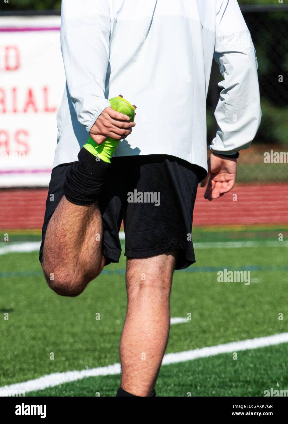 Ein High-School-Fußballspieler hält ein Bein bis zu seinem, aber um seinen Quad vor einem Spiel zu Strecken. Stockfoto