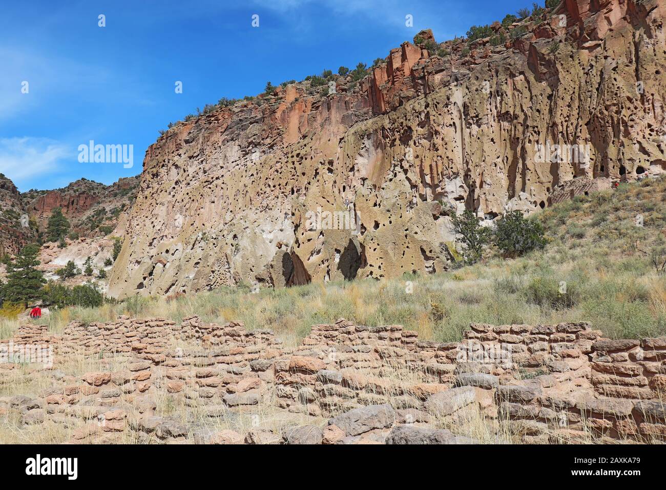 Ein Teil der Tyuonyi-Ruinen der angestammten Pueblo-Völker ist ein nicht identifizierbarer Wanderer an den Klippen entlang des Hauptschleifenweges im Frijoles Canyon bei Bande Stockfoto