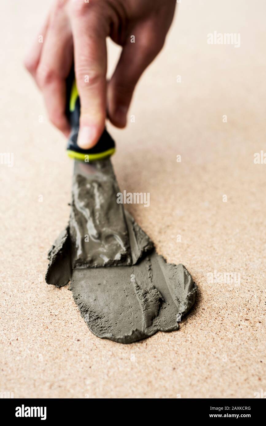 Nahaufnahme des kaukasischen Mannes, der etwas Beton mit einem Schaber auf einer Faserplattenoberfläche spreizt Stockfoto