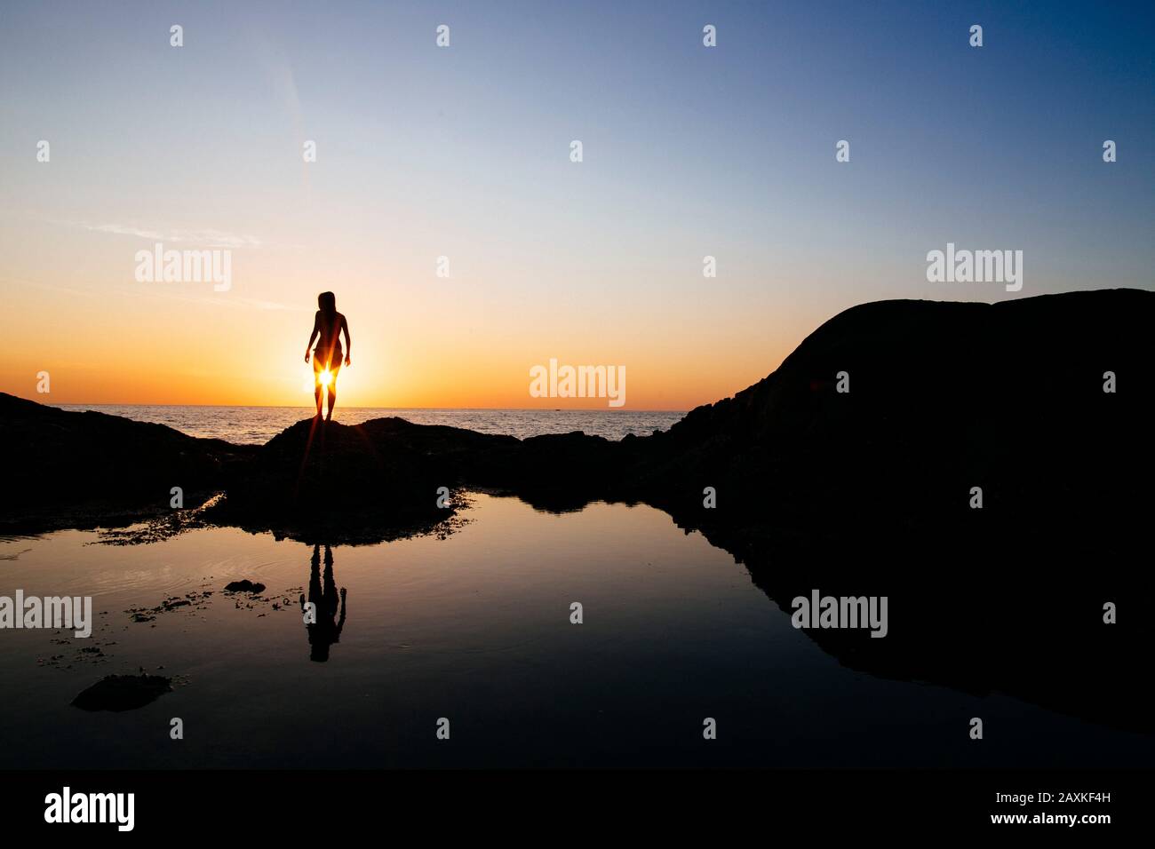 Silhouette der Frau, die bei Sonnenuntergang auf einem Felsen am Meer steht. Stockfoto