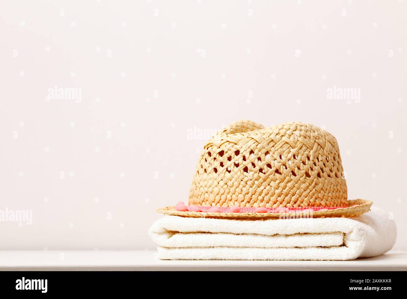 Sommerfrische am Strand, Strohhut und ein Handtuch auf dem Tisch im Hintergrund von hellen Wänden. Stockfoto