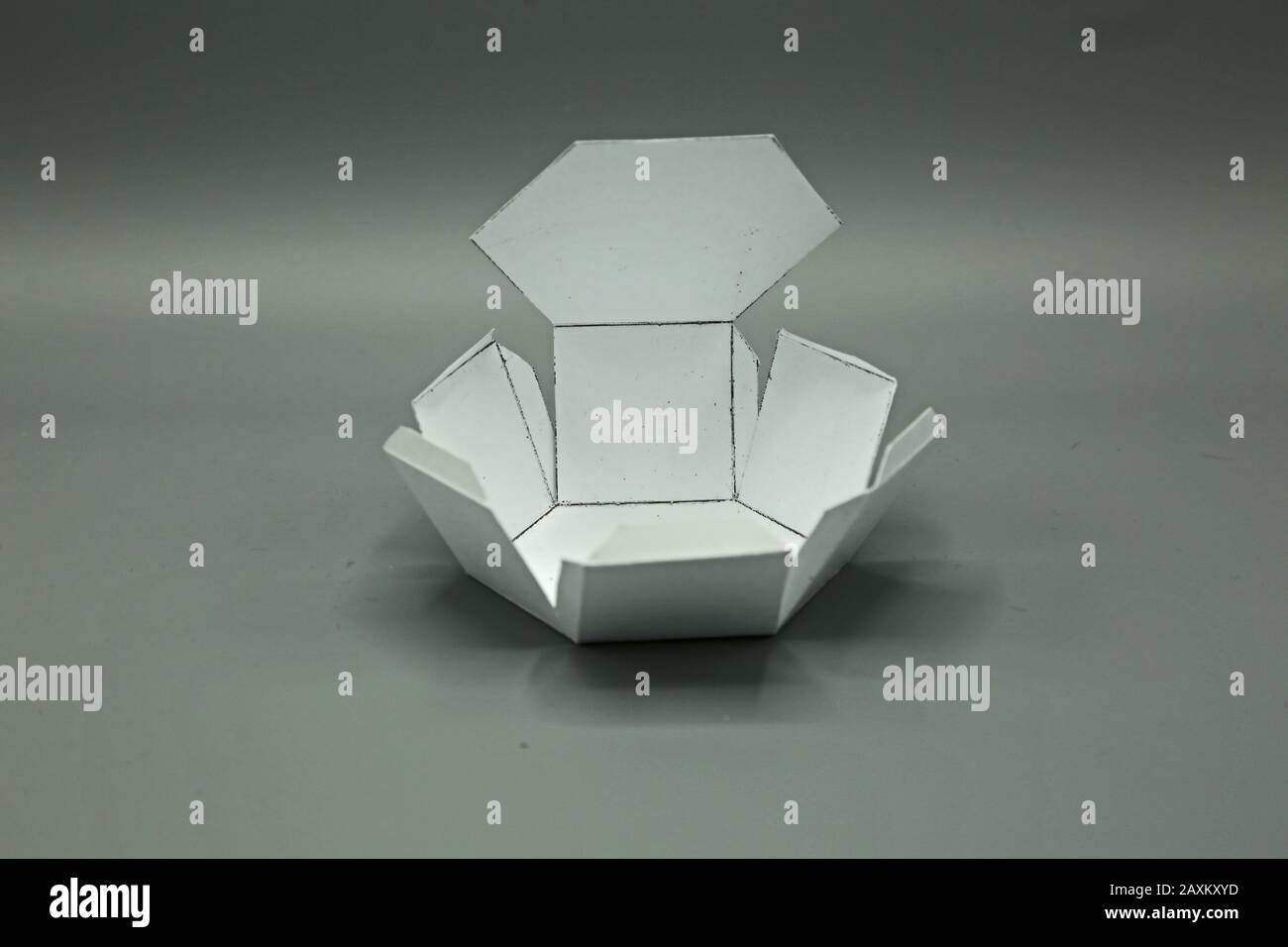 Geometrische Form aus Papier geschnitten und auf grauem Hintergrund fotografiert.Sechseckiges Prisma. 2-dimensionale Form faltbar, um eine 3D-Form oder einen Volumenkörper zu bilden. Unfo Stockfoto