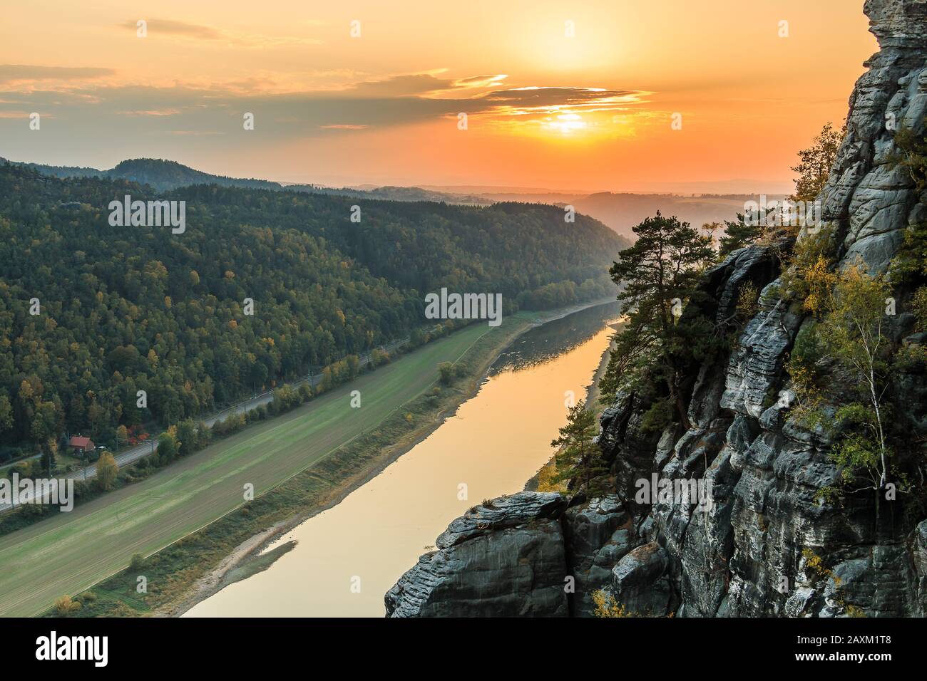Blick auf das Elbtal im Nationalpark Sächsische Schweiz. Elbe bei Sonnenuntergang. Farbenfroher Himmel mit gelb-roter Sonne. Landschaft mit Felsen, Bäumen Stockfoto