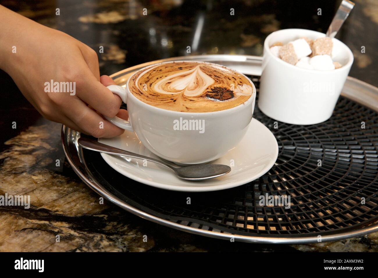 Die Hand einer Frau ist dabei, eine Tasse Cappuccino-Kaffee zu heben. Stockfoto