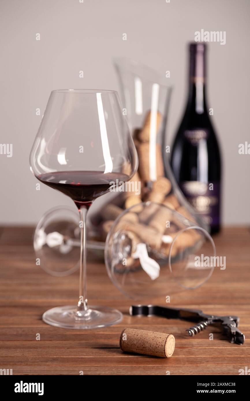 Glas Rotwein, Flasche, Korkenzieher, Dekanter mit Korken auf Holztisch, Nahaufnahme, vertikaler, selektiver Fokus, Seitenansicht, Kopierraum Stockfoto