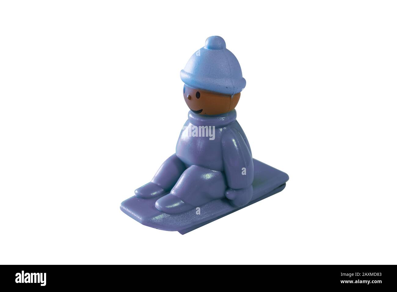 Kleines buntes Spielzeug für kleine Kinder eines Kindes, das auf einem Schlitten sitzt, der den Hügel hinuntergeht, mit einem Hut gegen die Kälte und den Fäusten, die eng am sitzen Stockfoto