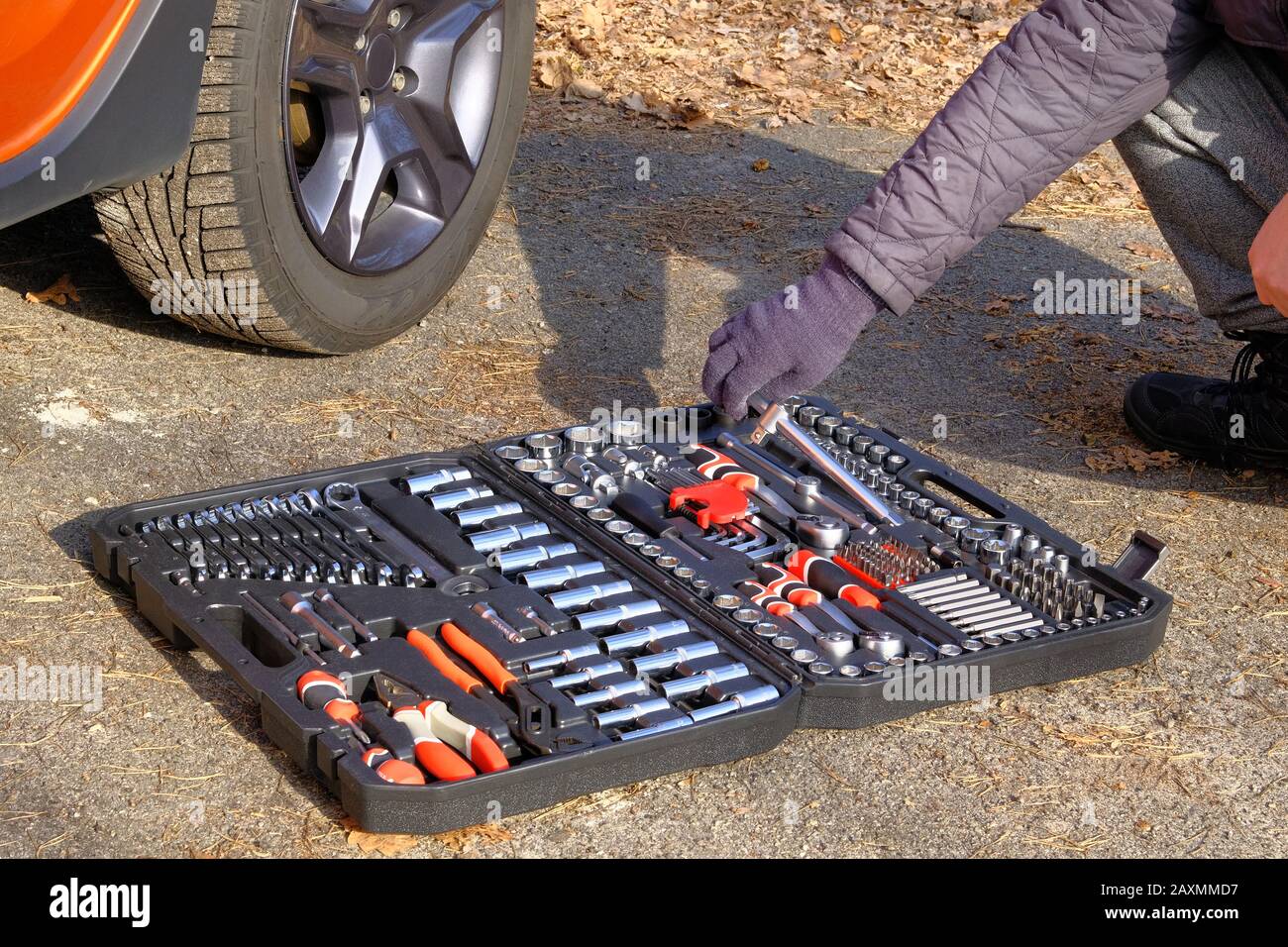 Werkzeugsatz in der Nähe des Auto. Mechanische Werkstattwerkzeuge im Karton. Сar Mechaniker verwenden verschiedene Reparaturwerkzeuge für die Reparatur eines orangefarbenen Autos. Stockfoto