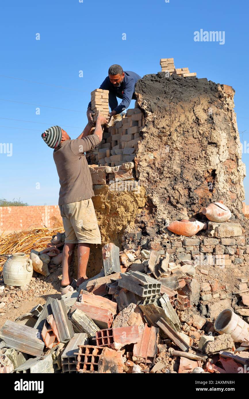Tozeur, TUNESIA - 20. DEZEMBER 2019: Zwei ortsansässige Arbeiter, die in einer Ziegelei in traditioneller Weise Backsteine bauen. Sie legen die getrockneten Backsteine in einen Ofen Stockfoto