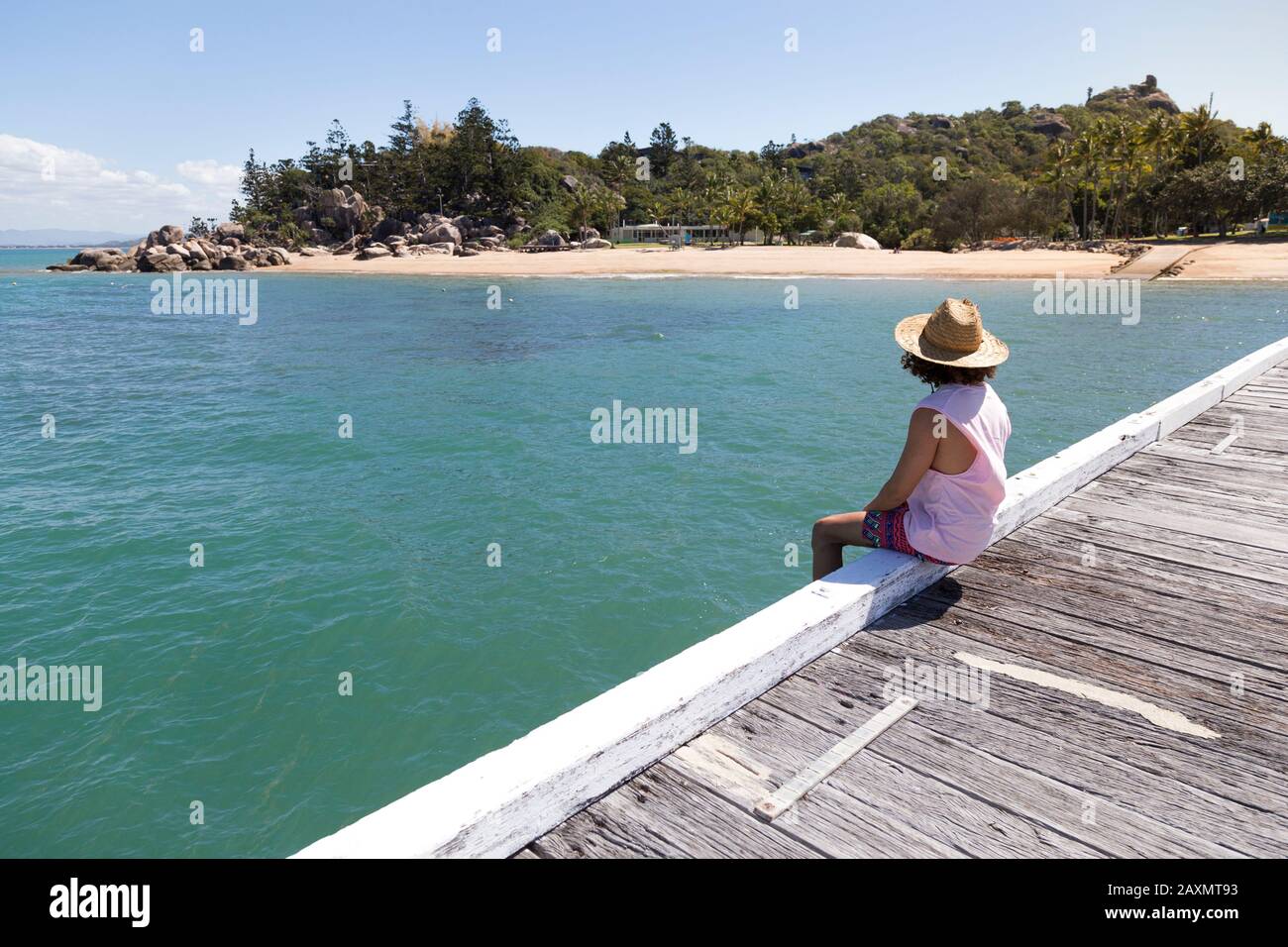 Lockiges Haar Mann, mit Sonnenhut, sitzt auf dem Rand des Holzdocks Stockfoto