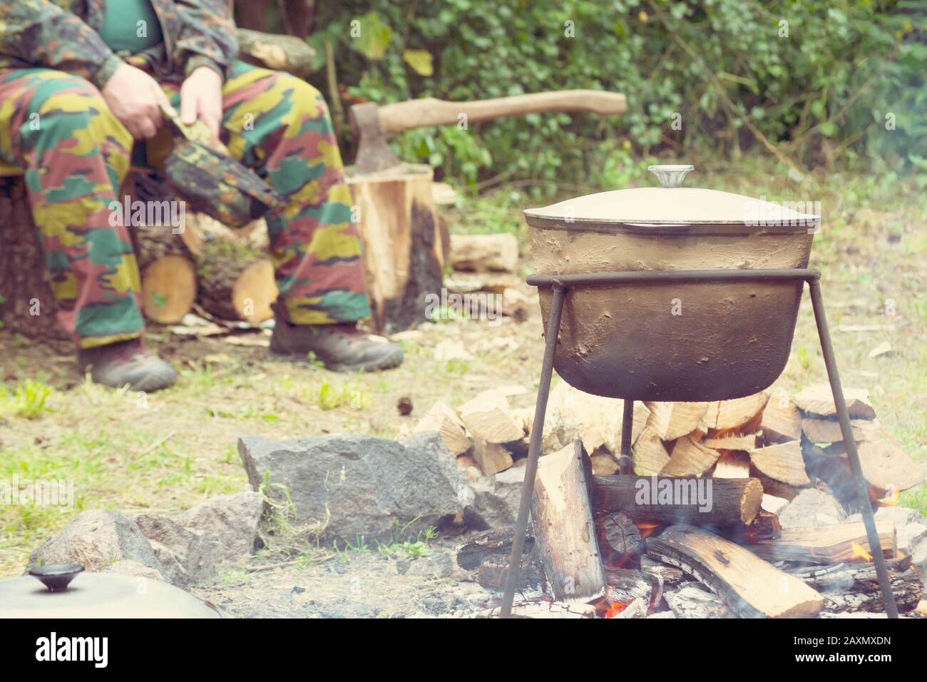 Mann in Tarnung in einem Wald in der Nähe des Lagertopfes auf dem Feuer sitzen Stockfoto