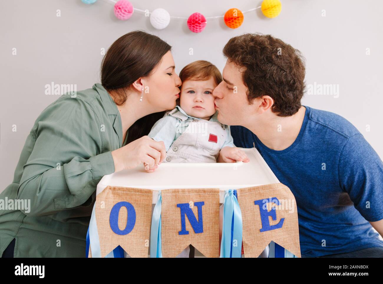 Kaukasische Familie mit Babyjungen, die zu Hause seinen ersten Geburtstag feiert. Vater der Mutter Vater Vater küsst Kind Kleinkind. Alles gute zum Geburtstag, authentisch Stockfoto