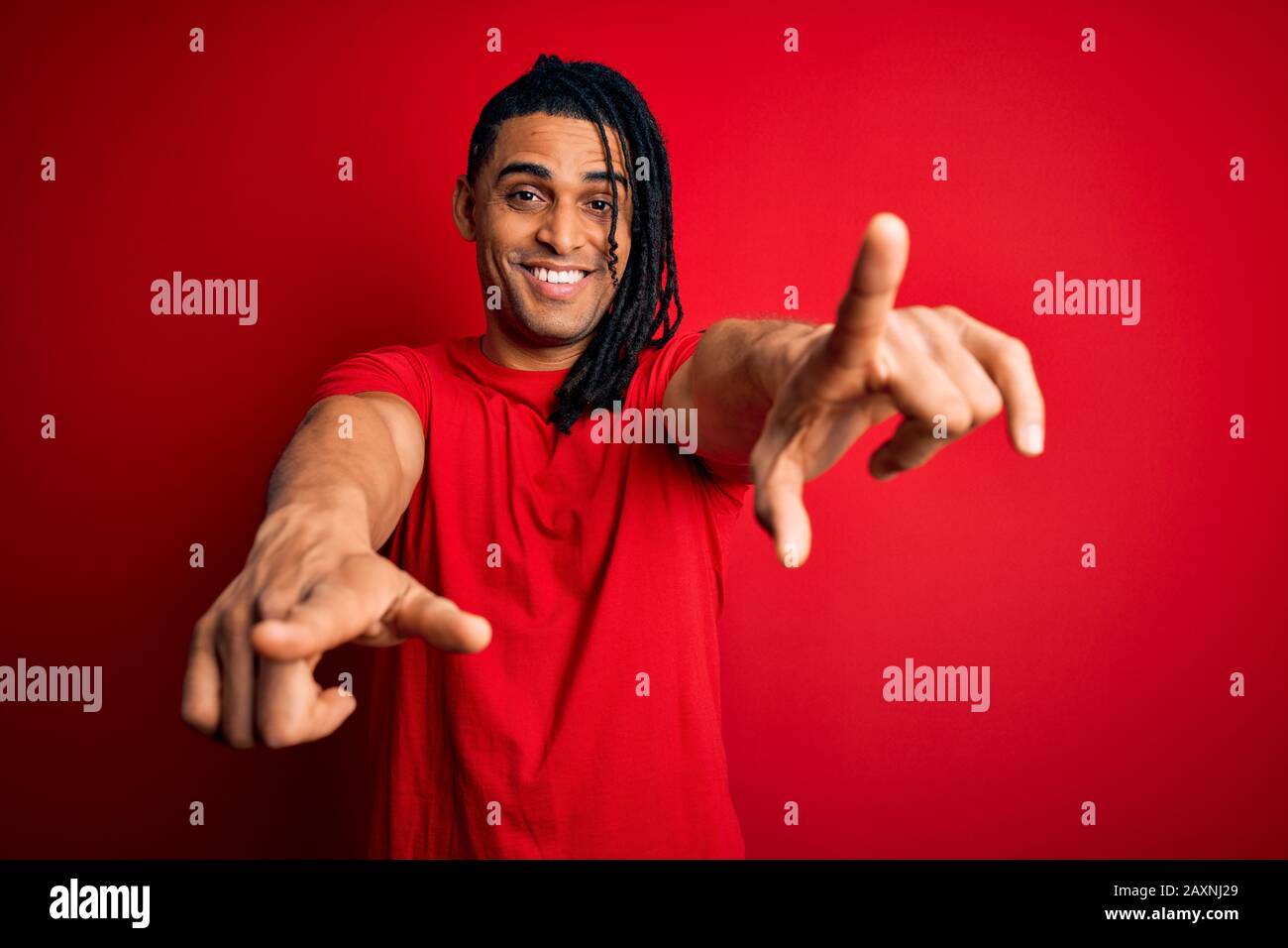 Junger, gutaussehender afro-amerikanischer afro-Mann mit Dreadlocks mit rotem Casual-T-Shirt, das auf Sie und die Kamera mit den Fingern zeigt, lächelnd positiv und Stockfoto