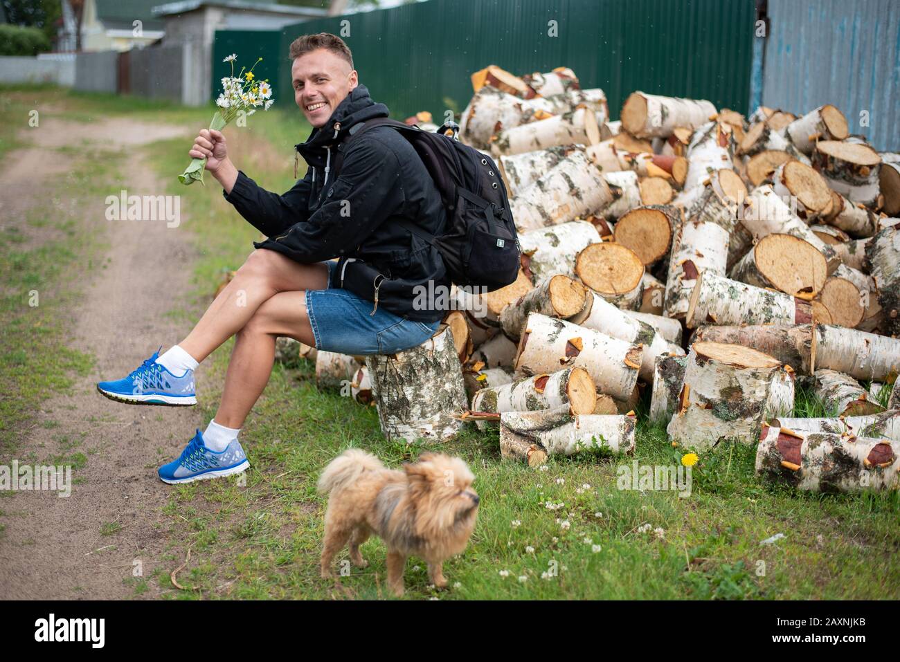 Ein städtischer Mann im Dorf, in der Nähe eines Haufens von Brennholz. Stockfoto