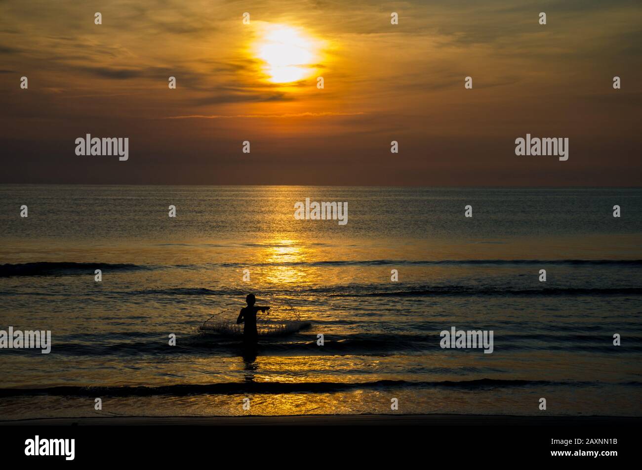 Silouhette von Fischern, die im Morgengrauen ein Netz in den Ozean werfen. Stockfoto