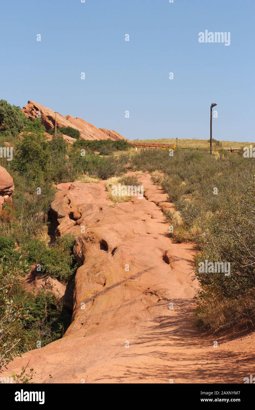 Red Rock Sandstein Wanderweg auf der Trading Post Trail in Red Rocks Park, Colorado, USA, umrandet mit Scheuerbürste, Gräser und Felsformationen in der Stockfoto