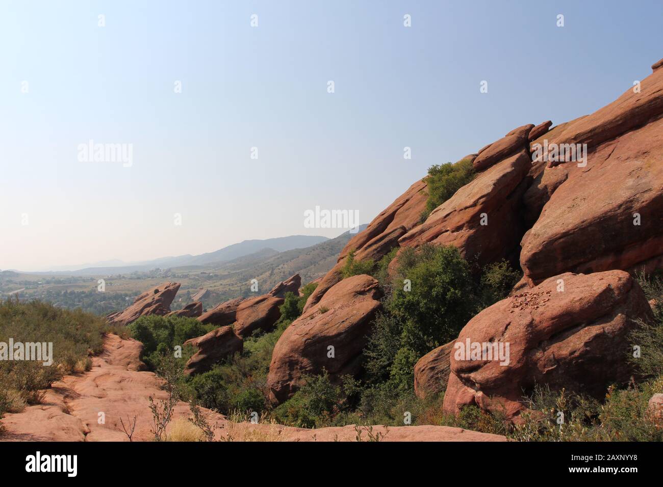 Ein Pfad neben großen Felsformationen aus rotem Sandstein mit Sträuchern, die in den Rissen auf dem Trading Post Trail im Red Rocks State Park, Morrison, wachsen Stockfoto