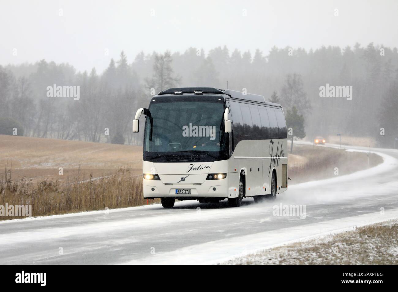 Weißer Volvo-Reisebus, der im Landstraßenverkehr im Winter-Schneefall unterwegs ist. Salo, Finnland. Februar 2020. Stockfoto