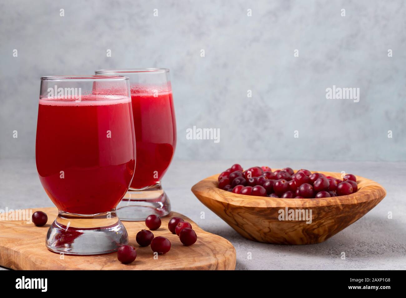 Zwei Gläser mit hausgemachtem, frisch gepresstem Preiselbeersaft und eine Schüssel mit Preiselbeeren auf einem grauen Betontisch. Stockfoto