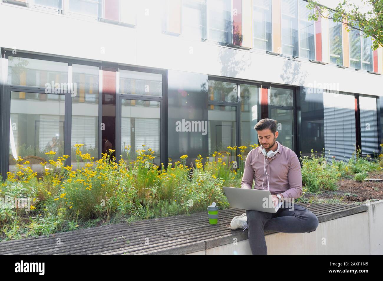 Junger Mann mit Laptop und Ohrhörer vor dem modernen Bürogebäude Stockfoto