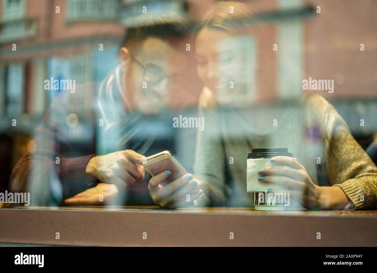 Junges glückliches Paar in der Kaffeebar, das Cappuccino trinkt und Spaß mit dem Handy hat - Fröhliche Leute genießen Zeit zusammen mit neuer Sozialtechnik Stockfoto