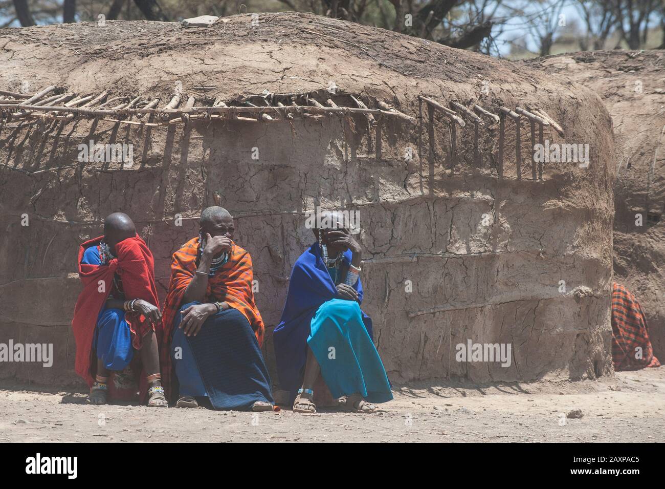 Drei Masai-Frauen sitzen vor einem traditionellen Dunghaus und schützen ihre Augen vor dem Staub. Stockfoto