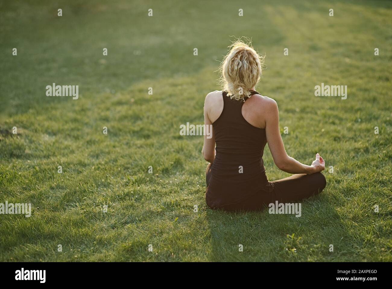Junge Frau, die Yoga in Meditationshaltung auf einer Matte im Garten macht. Stockfoto