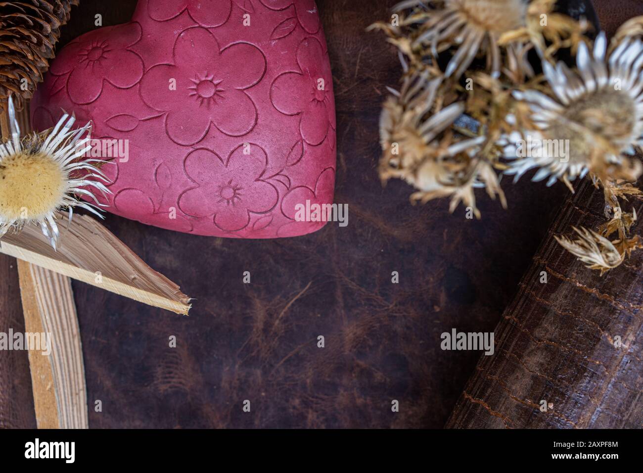 Valentinstag, rosafarbenes geblümtes Herz mit Strohblumen und Anzünden auf Lederhintergrund. Hochwinkelansicht für Text. Stockfoto