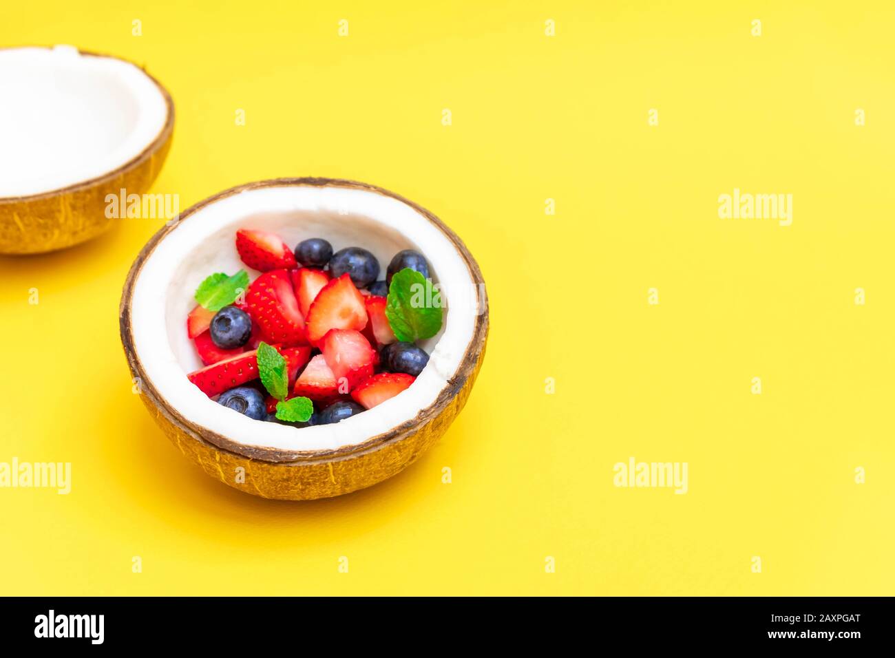 Kokospalschüssel mit frischen Beeren auf gelbem Hintergrund mit Kopierraum Stockfoto