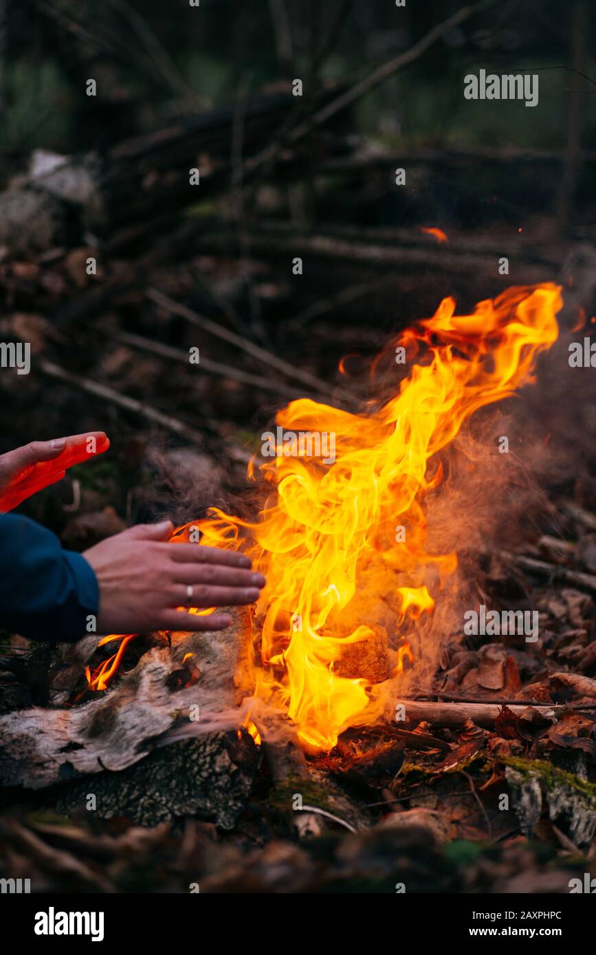 Der Mensch wärmt seine Hände auf Feuer. Brennendes Holz am Abend im Wald. Lagerfeuer im touristischen Camp in der Natur. Grillen und Kochen im Freien frische Luft Stockfoto