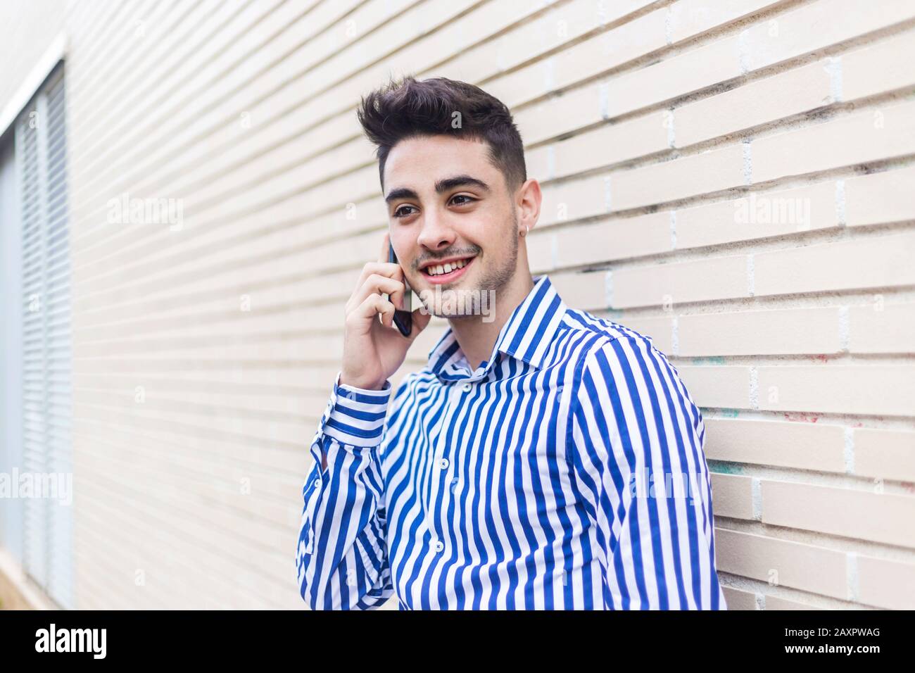 Porträt eines gutaussehenden jungen Mannes, der draußen steht, während er sein Handy auf der Straße benutzt. Stockfoto