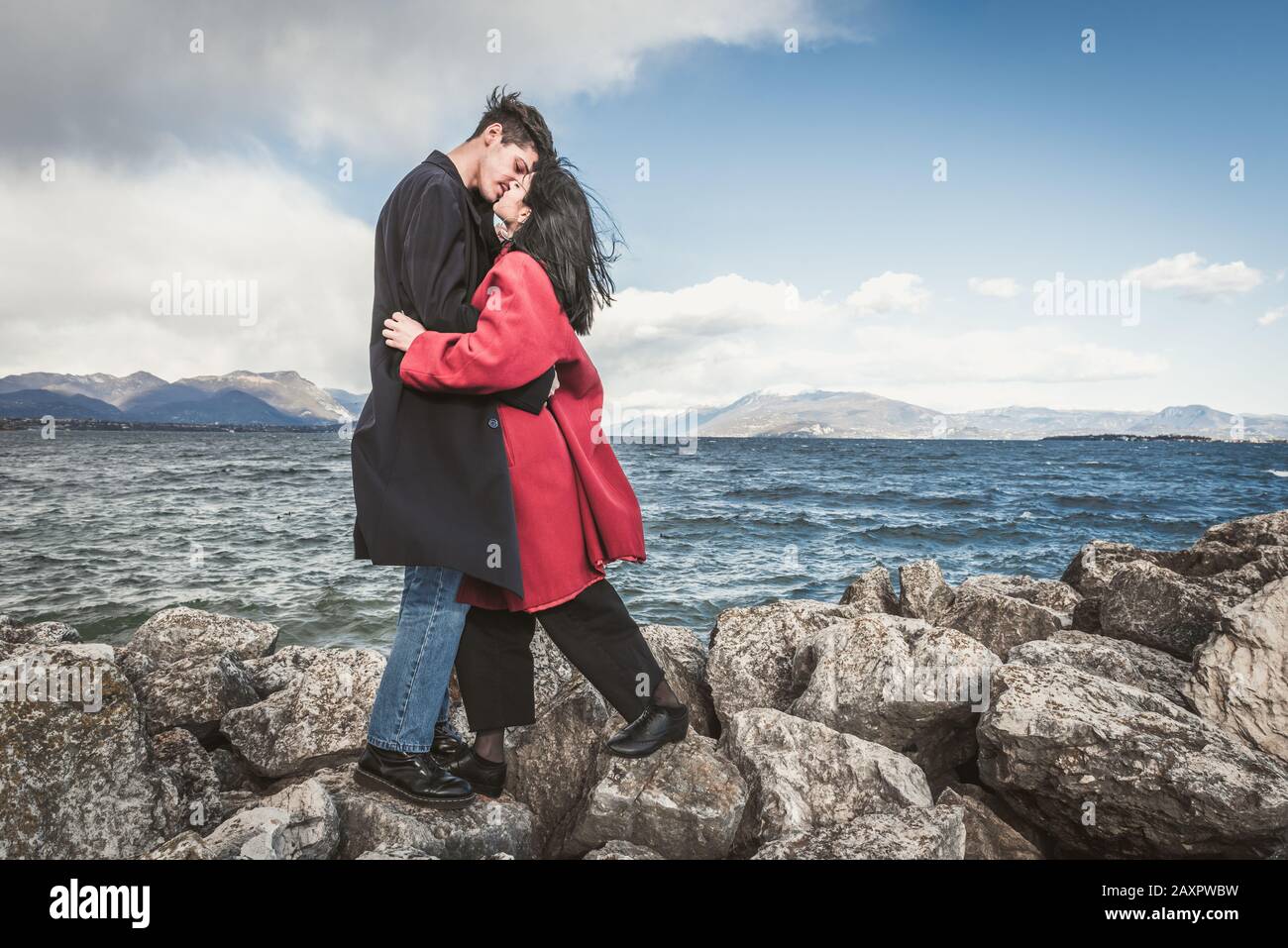 Liebevolle Paare, küssen sich vor dem Hintergrund des Sees und der Berge. Küssender brünette Mann und braunhaarige Frau im Freien Stockfoto