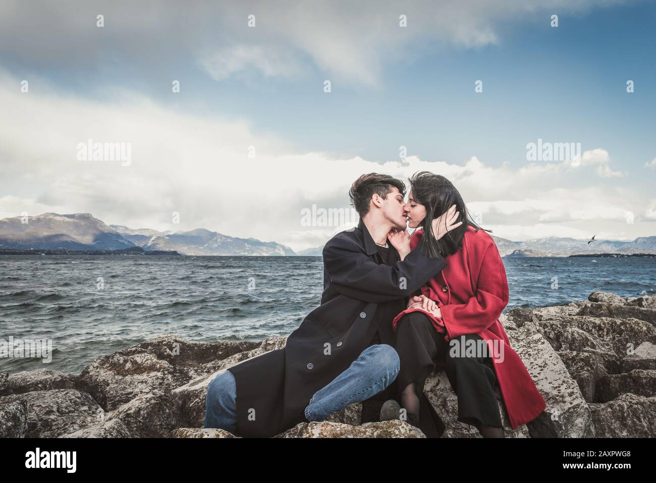 Liebevolle Paare, küssen sich vor dem Hintergrund des Sees und der Berge. Küssender brünette Mann und braunhaarige Frau im Freien Stockfoto
