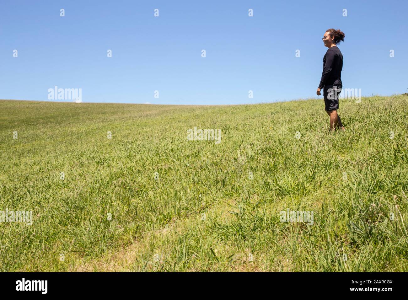 Tourist mit Shorts, Sonnenbrille und schwarzem Hemd, auf grünem Grasland Stockfoto