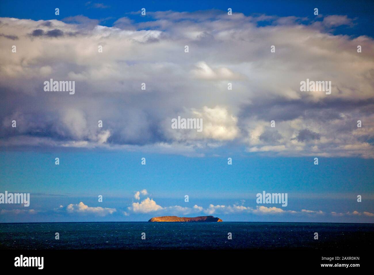 Blick auf ein bewölkter Himmel über eine ruhige See mit einer Insel am Horizont. Stockfoto
