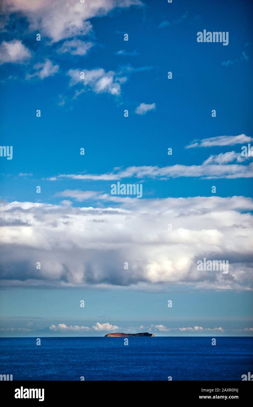 Blick auf ein bewölkter Himmel über eine ruhige See mit einer Insel am Horizont. Stockfoto
