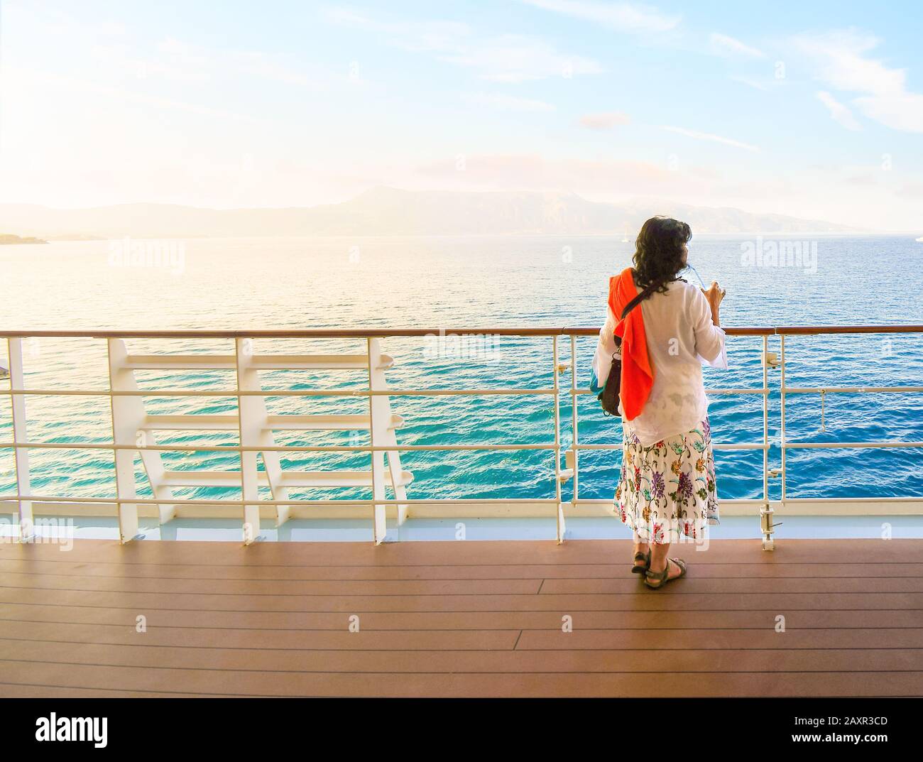 Eine junge Brunette-Frau genießt bei Sonnenaufgang ein Getränk auf dem Außendeck eines Kreuzfahrtschiffs im Mittelmeer. Stockfoto