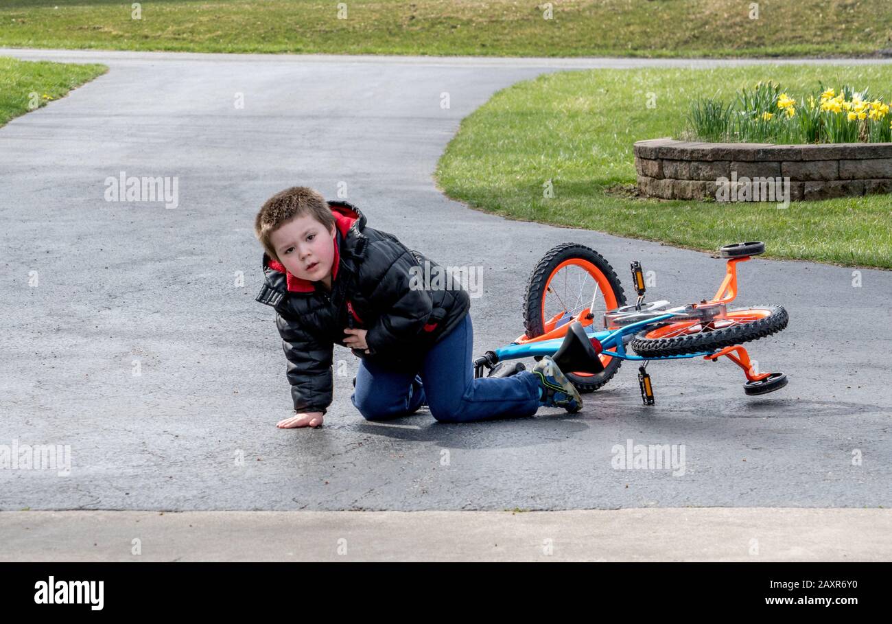 Kleiner Junge, der in der Einfahrt der Familie von einem Fahrrad abfällt Stockfoto