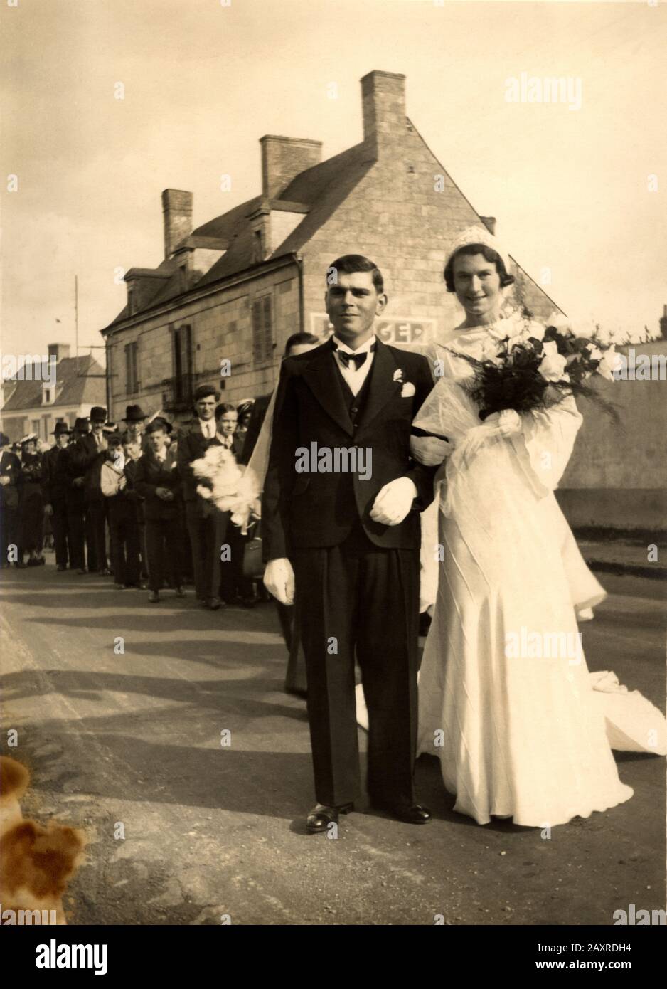 1940 Ca, SAUMUR, Maine-et-Loire, FRANKREICH: EINE Hochzeitsfeier, die nach der religiösen Zeremonie der Kirche in die Straße eindeichte. Foto von Studio Jean Decker, Saumur . - NOZZE - abito bianco da SPOSA - SPOSI - SPOSO - Handschuhe - Guanti - Blumen - fiori - Mazzo di Rose - Corteo in strada per la via - invitrati - ricevimento - MARITO E MOGLIE - HOCHZEITSKLEIDPARTY - BRIDE - Cerimonia - FOTO STORICHE - HISTORIENFOTOS - XX JAHRHUNDERT - NOVECENTO - Thulle - Tülle - Strascico - FAMIGLIA - FAMILIE - PARTI - festa - ricevimento - velo - Schleier - Blumen - fiori - fiore - Lächeln - sorriso - ARCHIVIO GBB Stockfoto