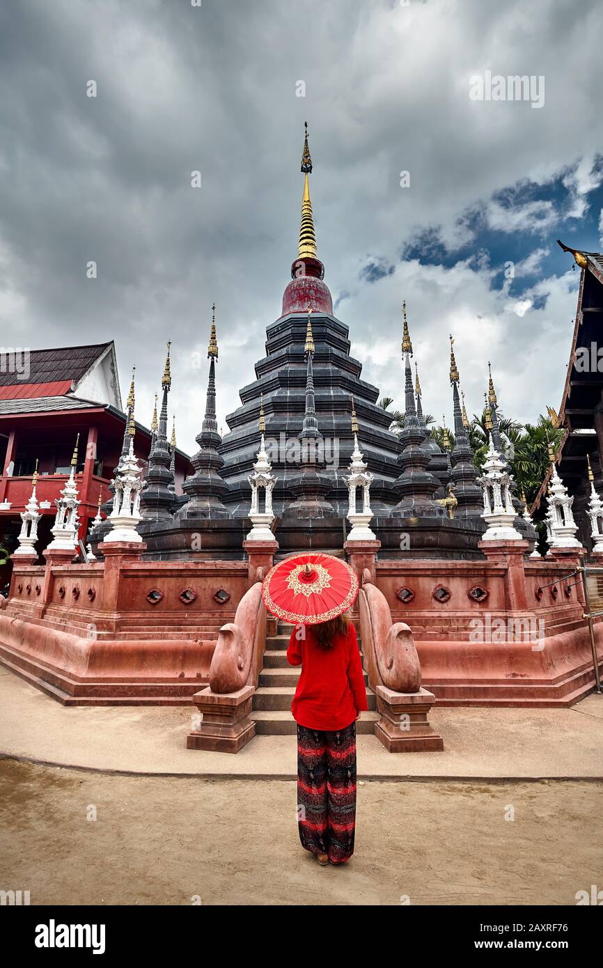 Frau mit rotem traditionellen thailändischen Regenschirm, die den schwarzen Tempel Wat Phan Tao in Chiang Mai, Thailand, betrachtet Stockfoto