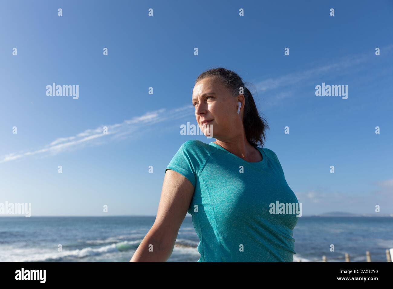 Seitenansicht einer erwachsenen kaukasischen Frau mittleren Alters, die an einer Promenade arbeitet, sich auf das Training vorbereitet und mit Ohrhörern wegschaut Stockfoto