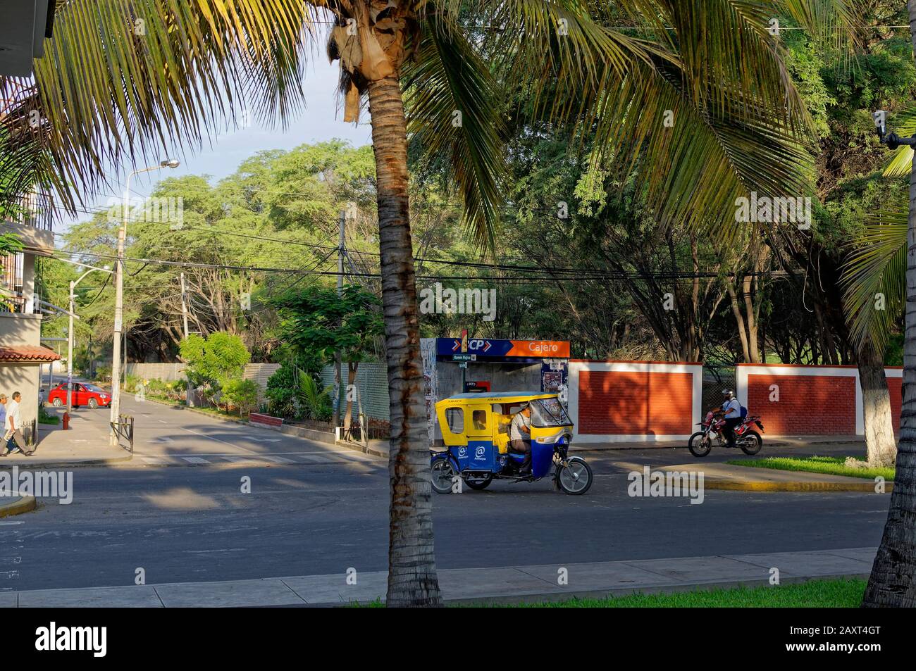 Ein Motorradtaxi, das aus einer Seitenstraße in der ländlichen Stadt Paita kommt und seine Passagiere im November an einem sonnigen Morgen zur Arbeit nimmt. Stockfoto