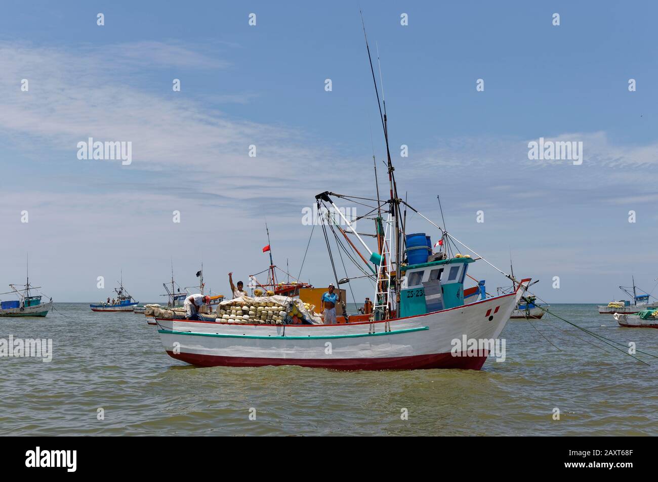 Fischer, die auf dem Deck eines verankerten peruanischen Küstenfischerboots arbeiten, winken, als ein Schiff vorbeifährt. Stockfoto