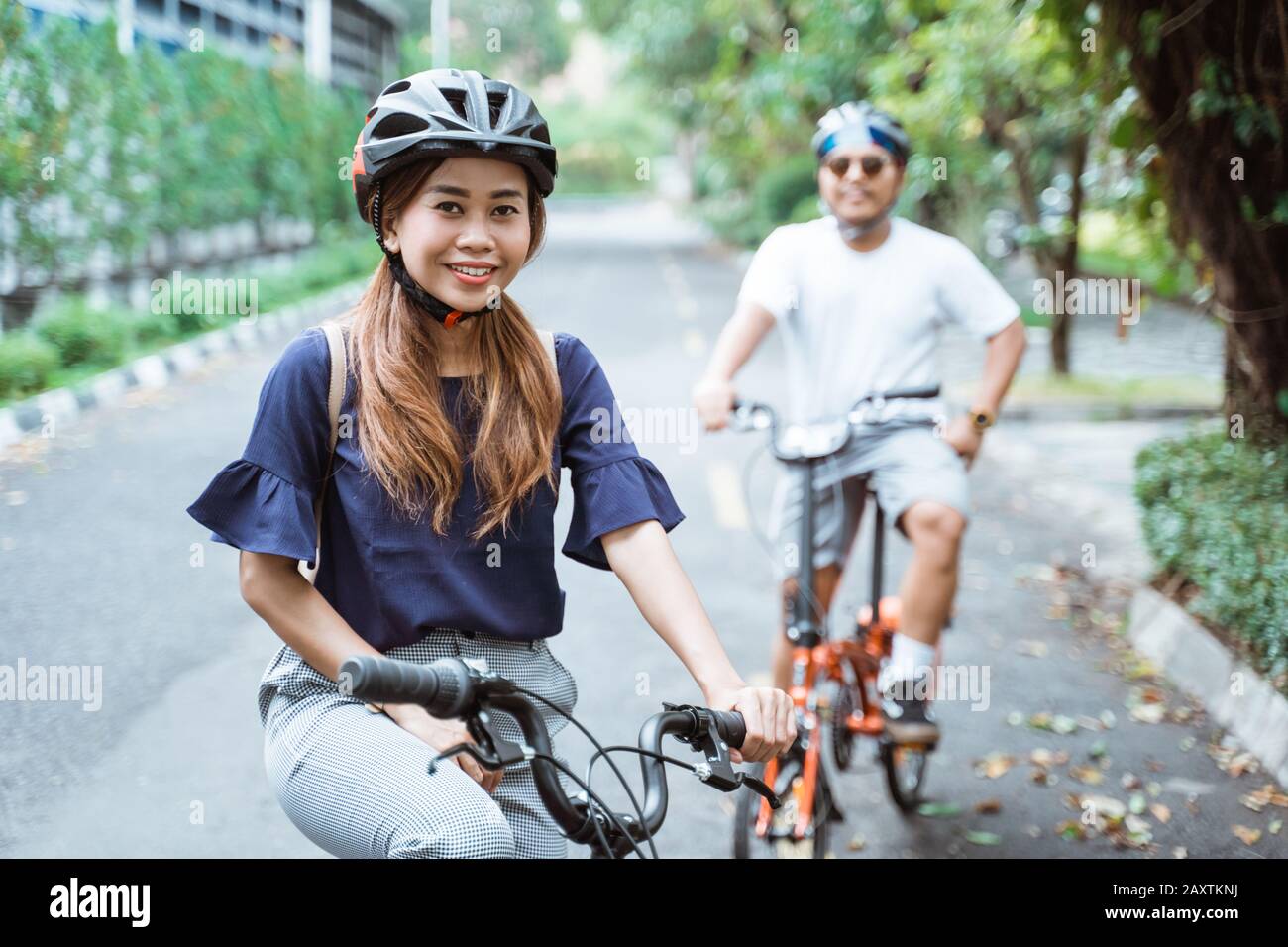 Junge asiatische Paare, die Helme tragen, genießen auf Reisen im Park das gemeinsame Fahrradfahren Stockfoto