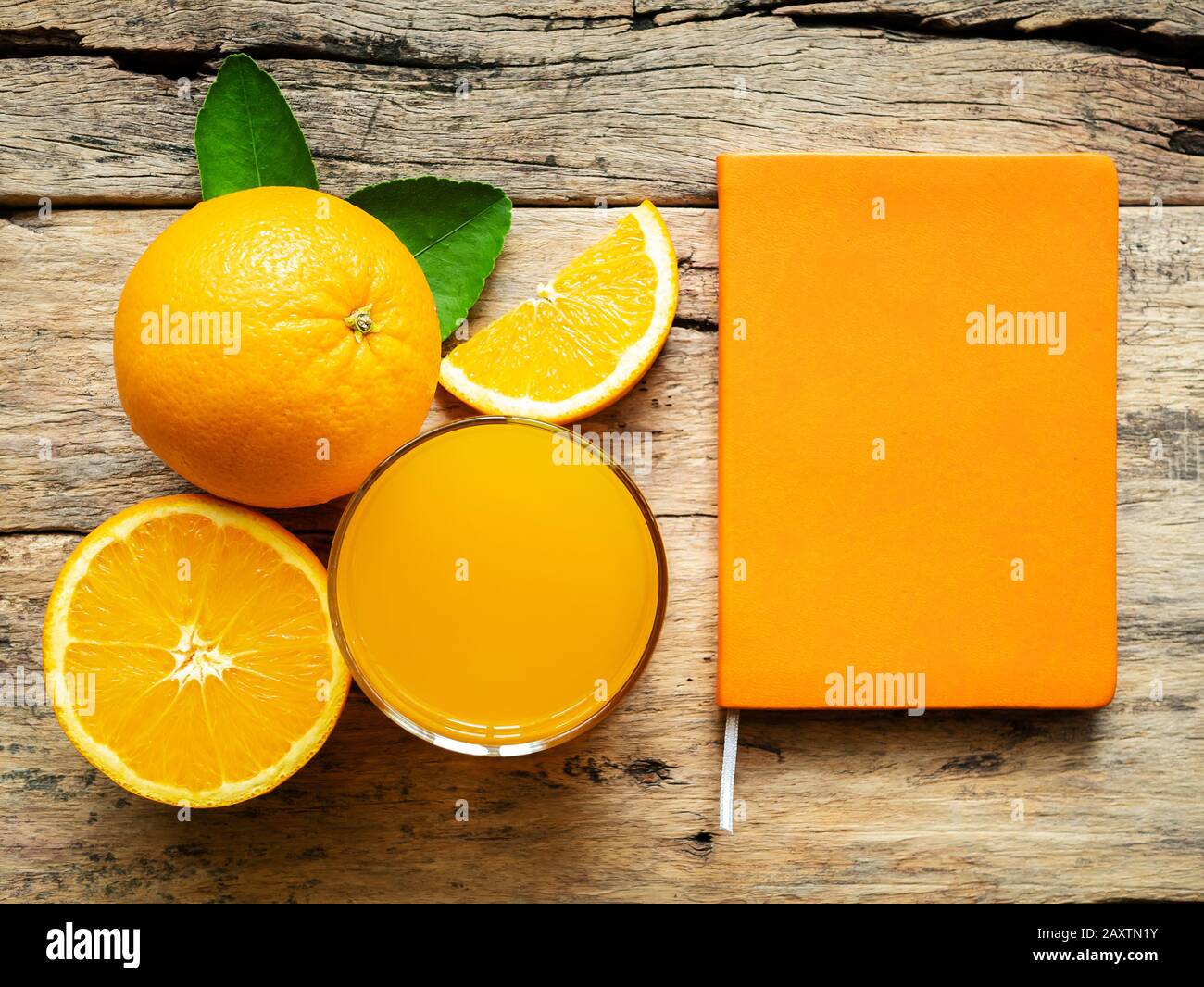 Ein Glas frischen Orangensaft und eine Gruppe frischer Orangenfrüchte mit grünen Blättern auf Holzhintergrund mit orangefarbener Buchfarbe. Vitamin C und fru Stockfoto