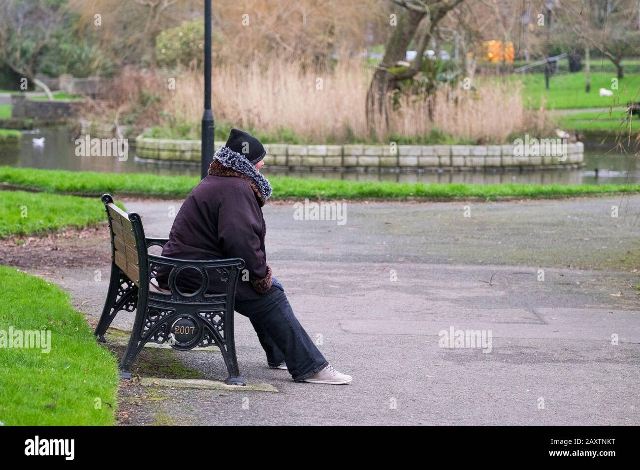Eine allein sitzende Frau auf einer Parkbank hat sich gegen das kalte Wetter gewickelt. Stockfoto
