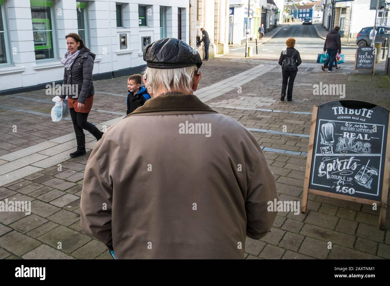 Die Rückansicht eines älteren Mannes, der eine Lederkappe trägt und Hörgeräte, die im Wadebridge Town Center in Cornwall laufen. Stockfoto