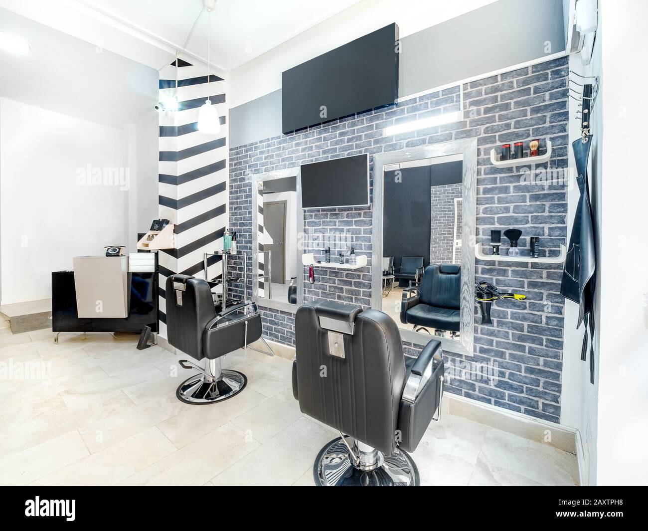 Moderner, heller Schönheitssalon. Friseursalon Innengeschäft mit minimalem Industrie-Look. Schwarz-weiße Einrichtung mit Spiegeln, Stühlen, tv-Bildschirm und m Stockfoto