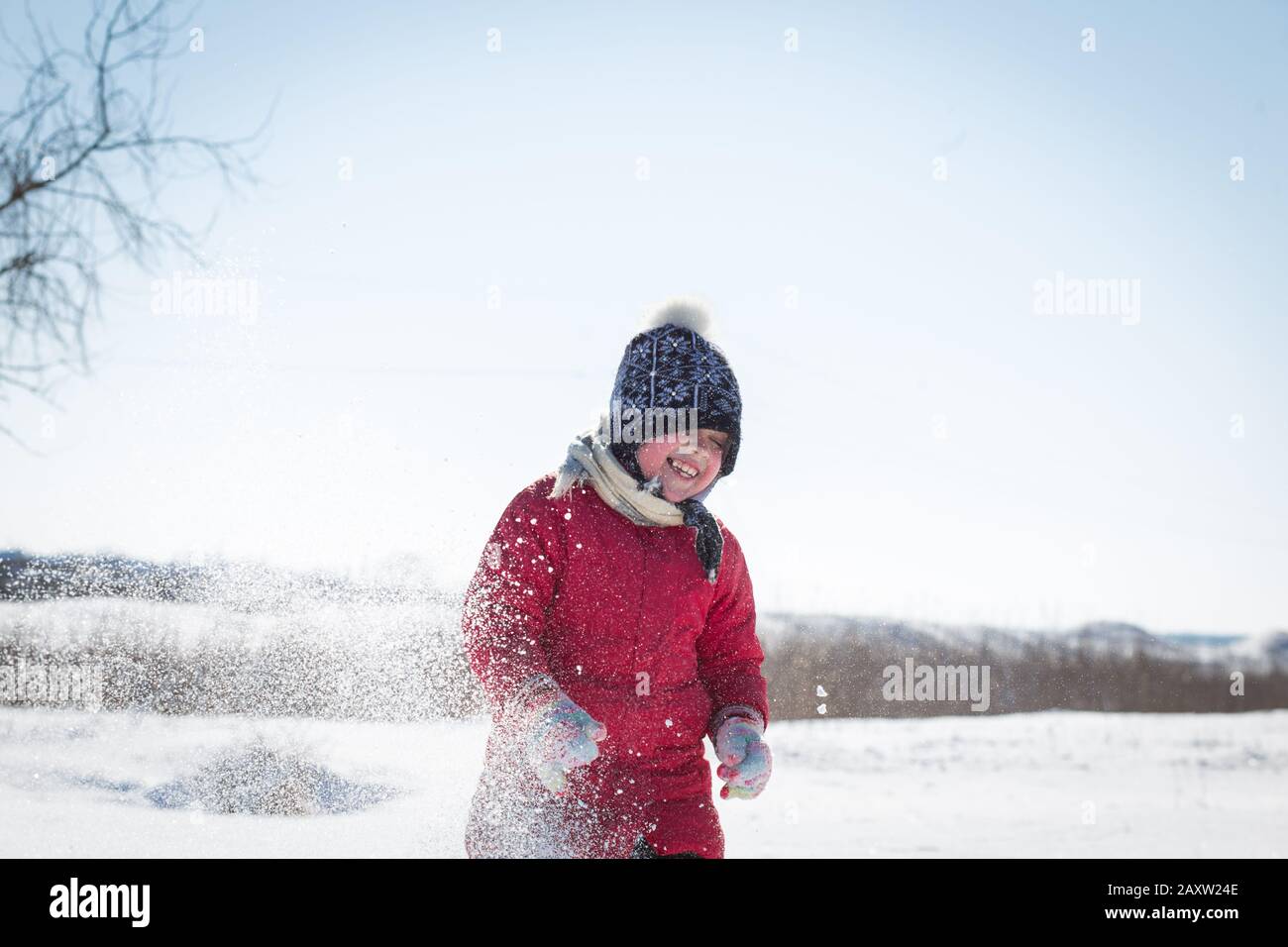 Kinder haben Spaß beim Schneewerfen. Das Mädchen ist warm gekleidet, schmeißt an einem frostigen sonnigen Tag Schnee. Stockfoto