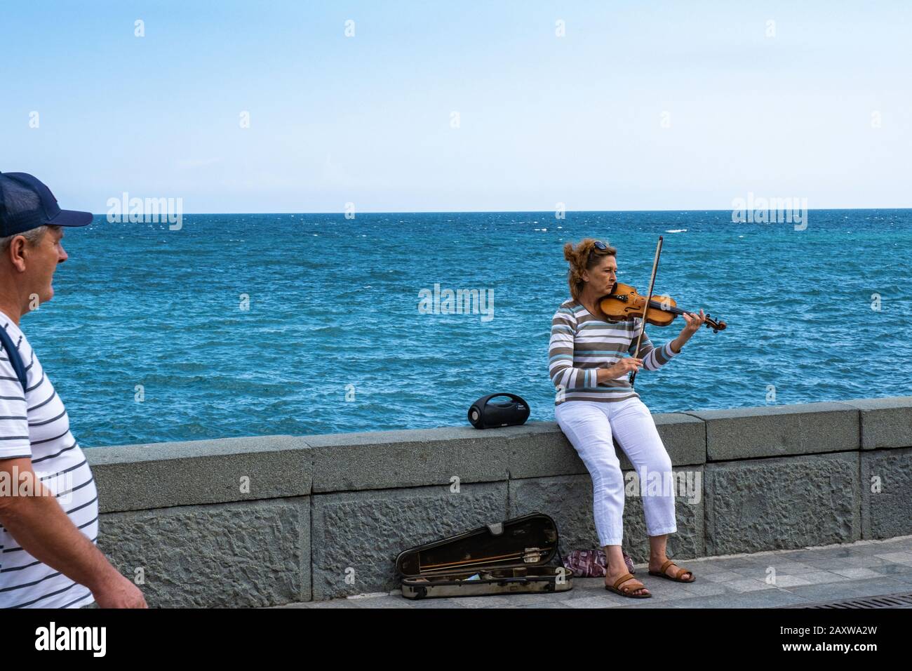 Jutta, Krim - 07.09.2019: Eine Frau in weißer Hose spielt vor dem Hintergrund des Meeres die Geige. Stockfoto