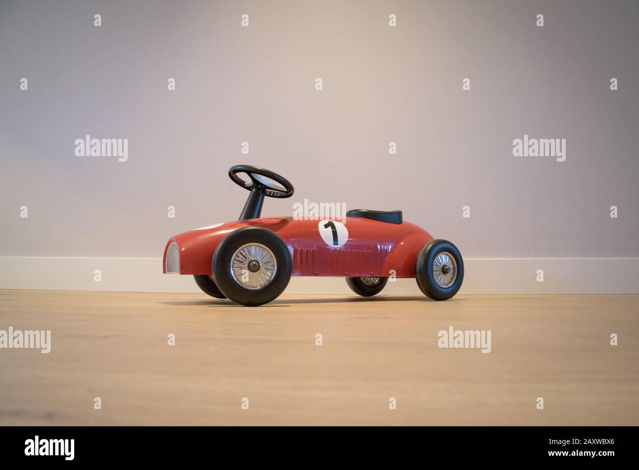 Oldtimer-roter Spielzeug-Rennwagen von Seite, gegen graue Wand und auf Holzboden Stockfoto